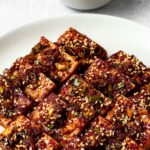 sliced korean braised tofu (dubu jorim) on a plate garnished with sesame seeds
