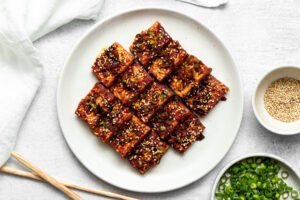 sliced korean braised tofu (dubu jorim) on a plate garnished with sesame seeds