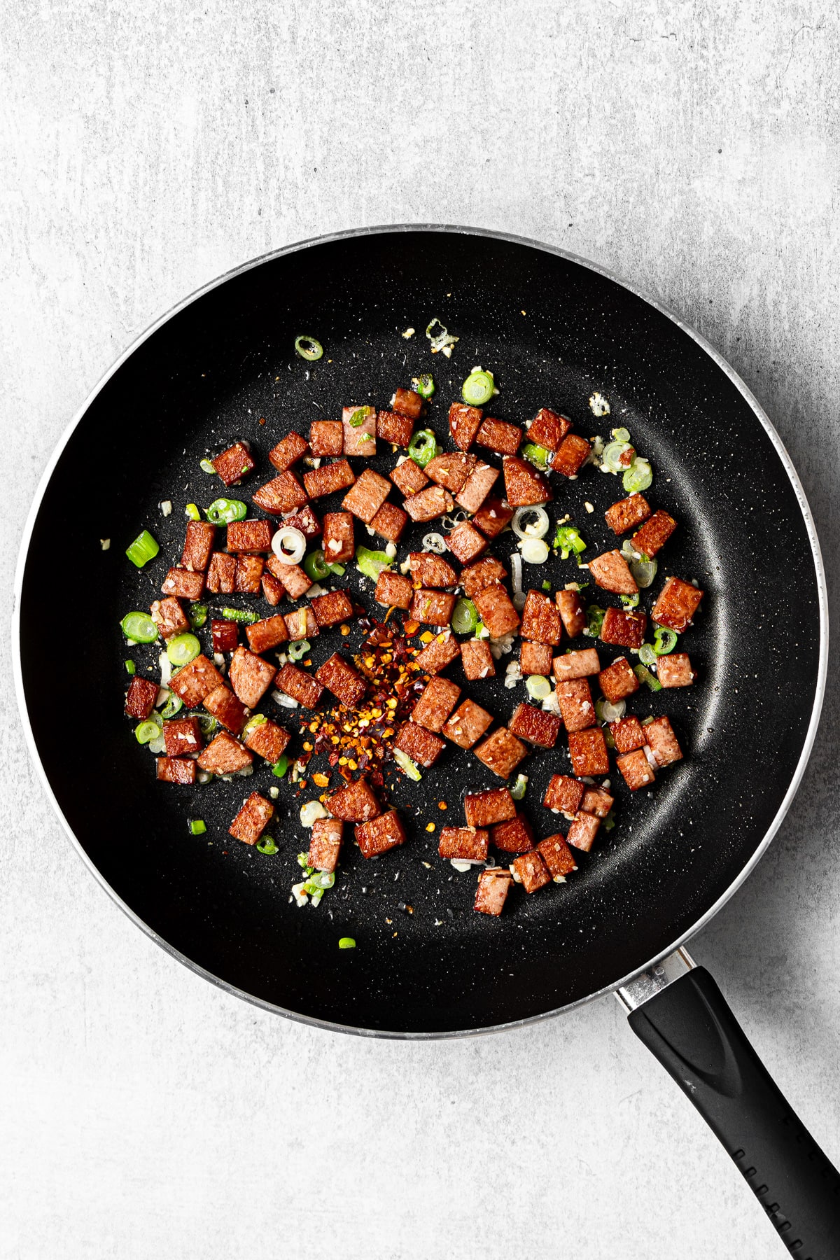 cooked spam and aromatics in a pan with red pepper flakes added