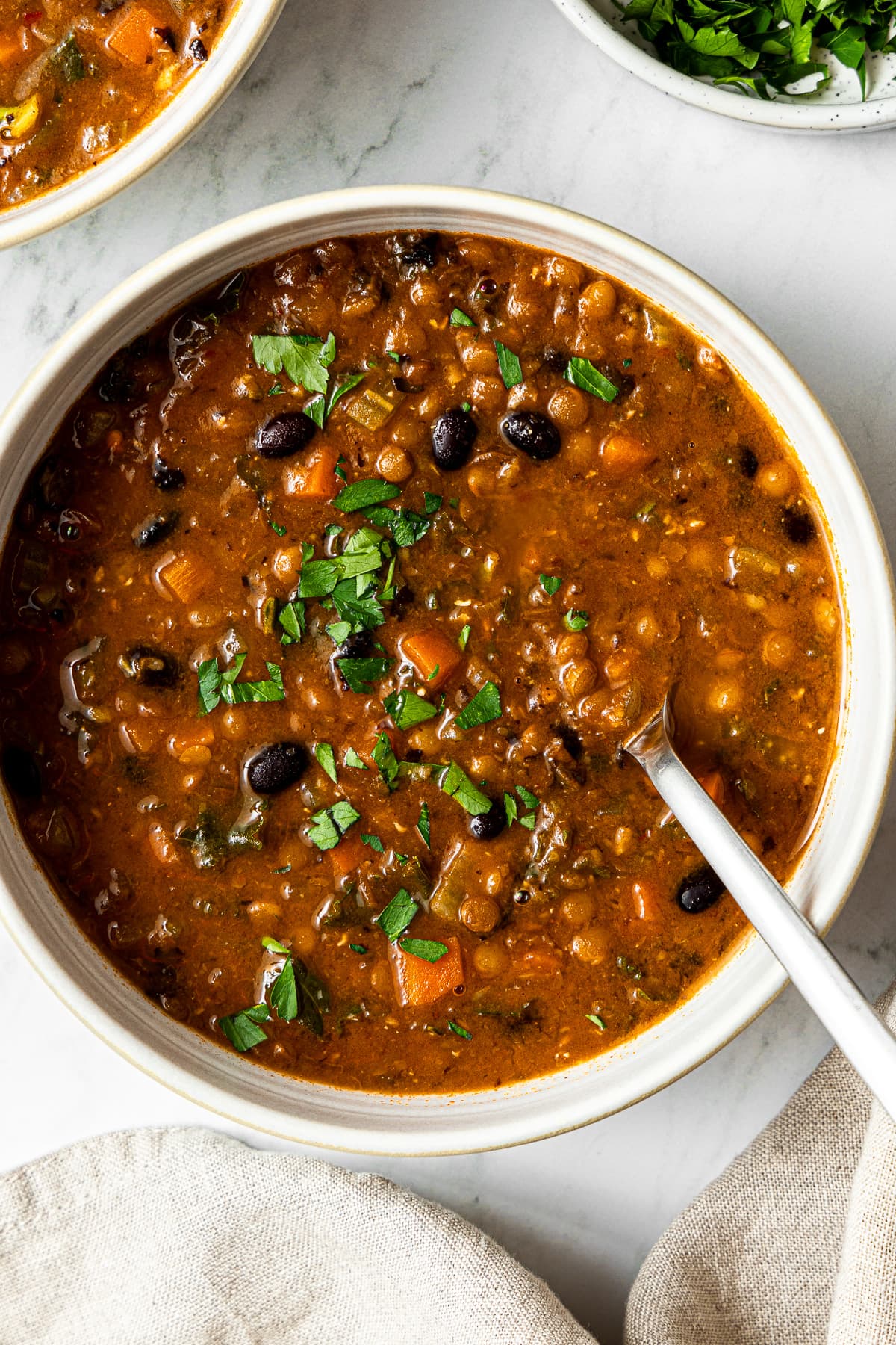 black bean and lentil soup garnished with chopped parsley in a bowl with a spoon