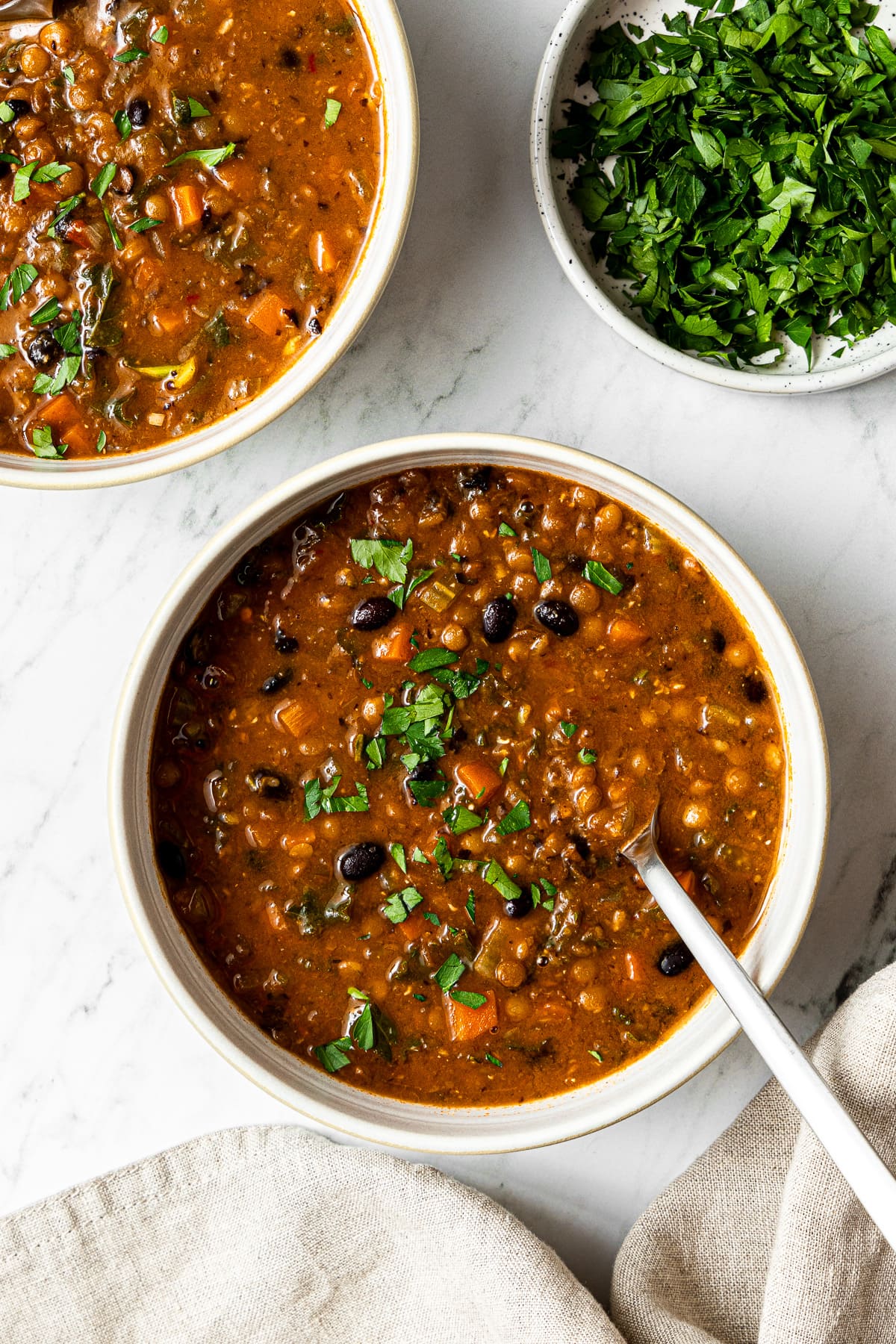 black bean and lentil soup garnished with chopped parsley in a bowl with a spoon