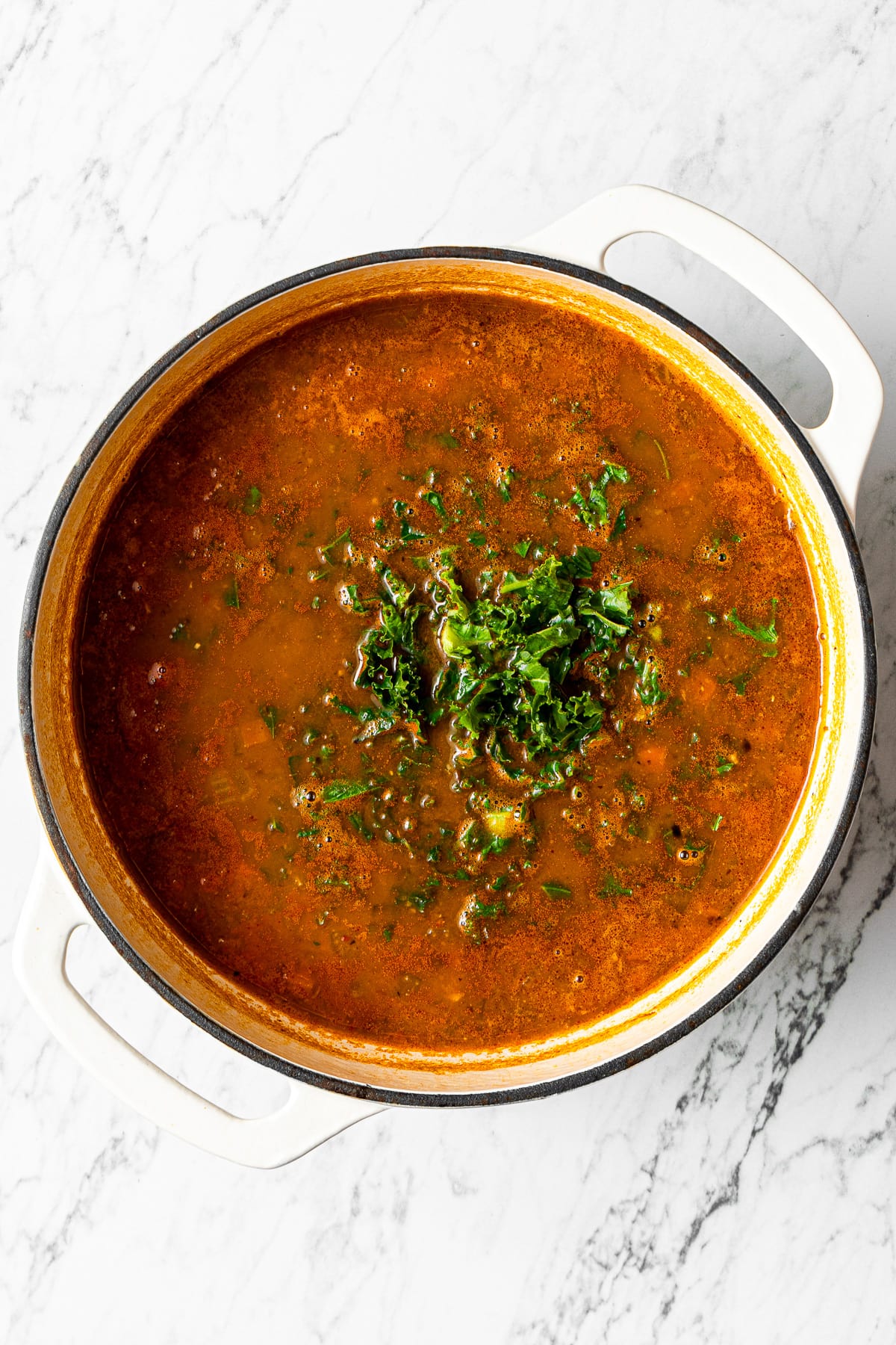 a large pot with black bean and lentil soup and some kale added to the pot