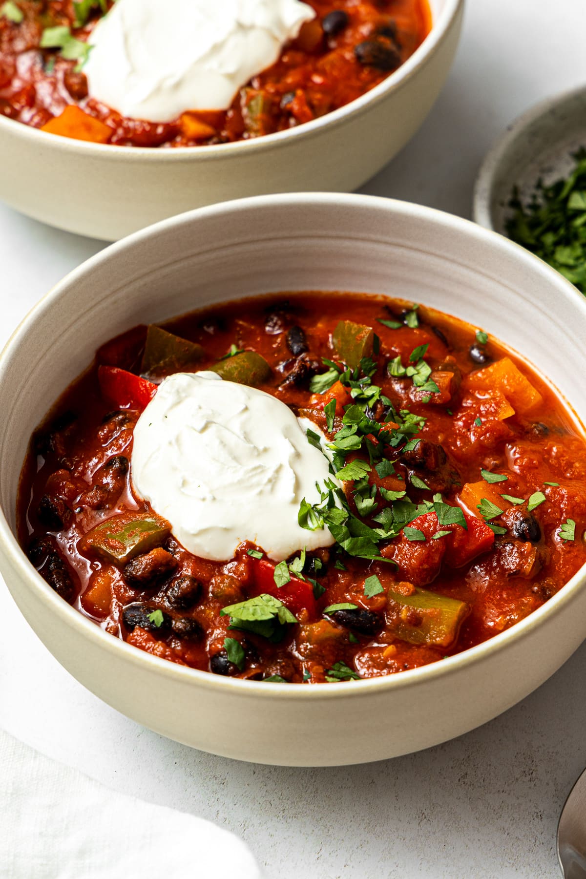 sweet potato black bean chili in a bowl garnished with chopped cilantro and sour cream
