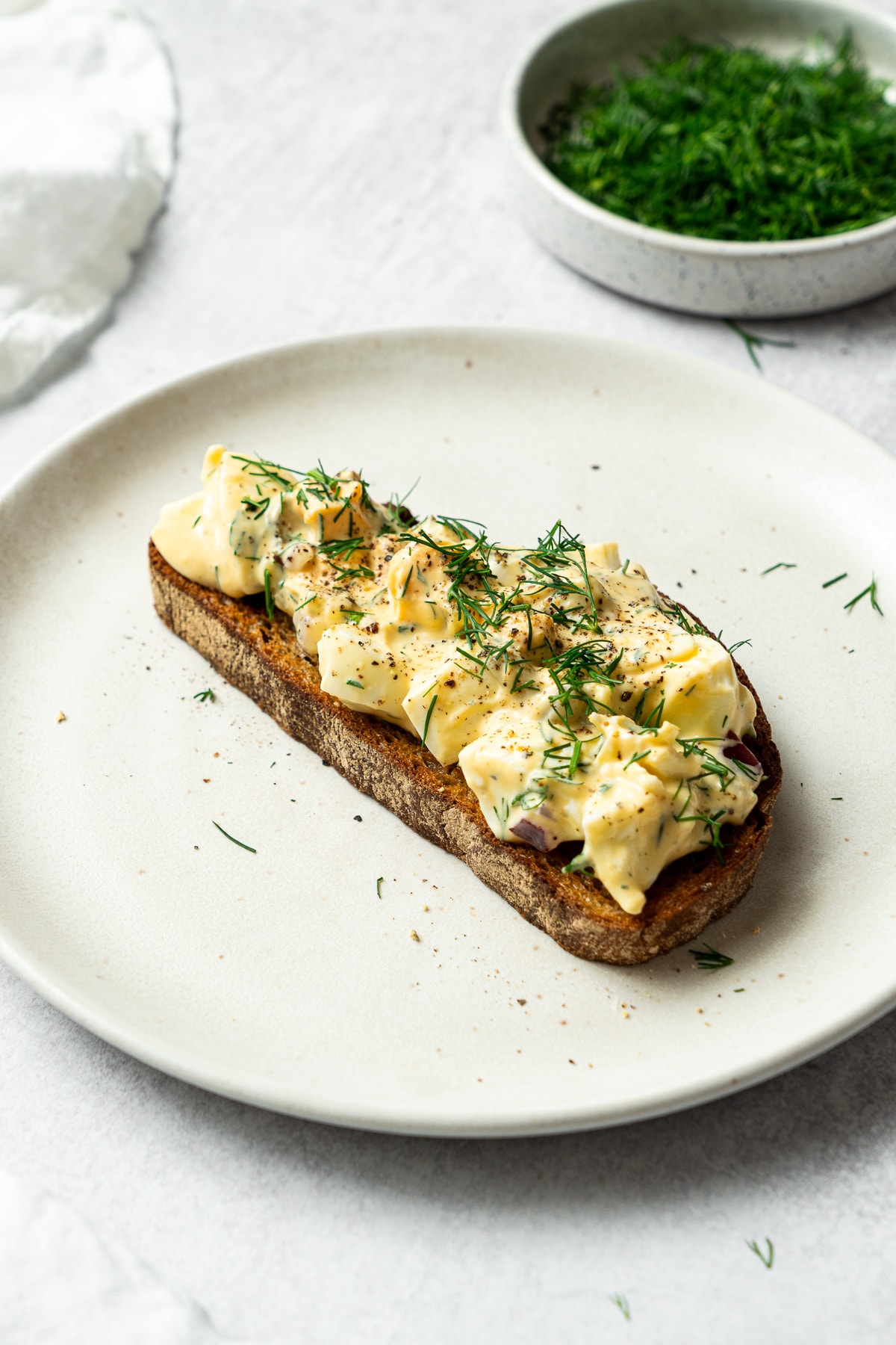 dill pickle egg salad garnished with chopped dill and black pepper on a slice of bread