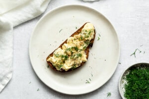dill pickle egg salad garnished with chopped dill and black pepper on a slice of bread