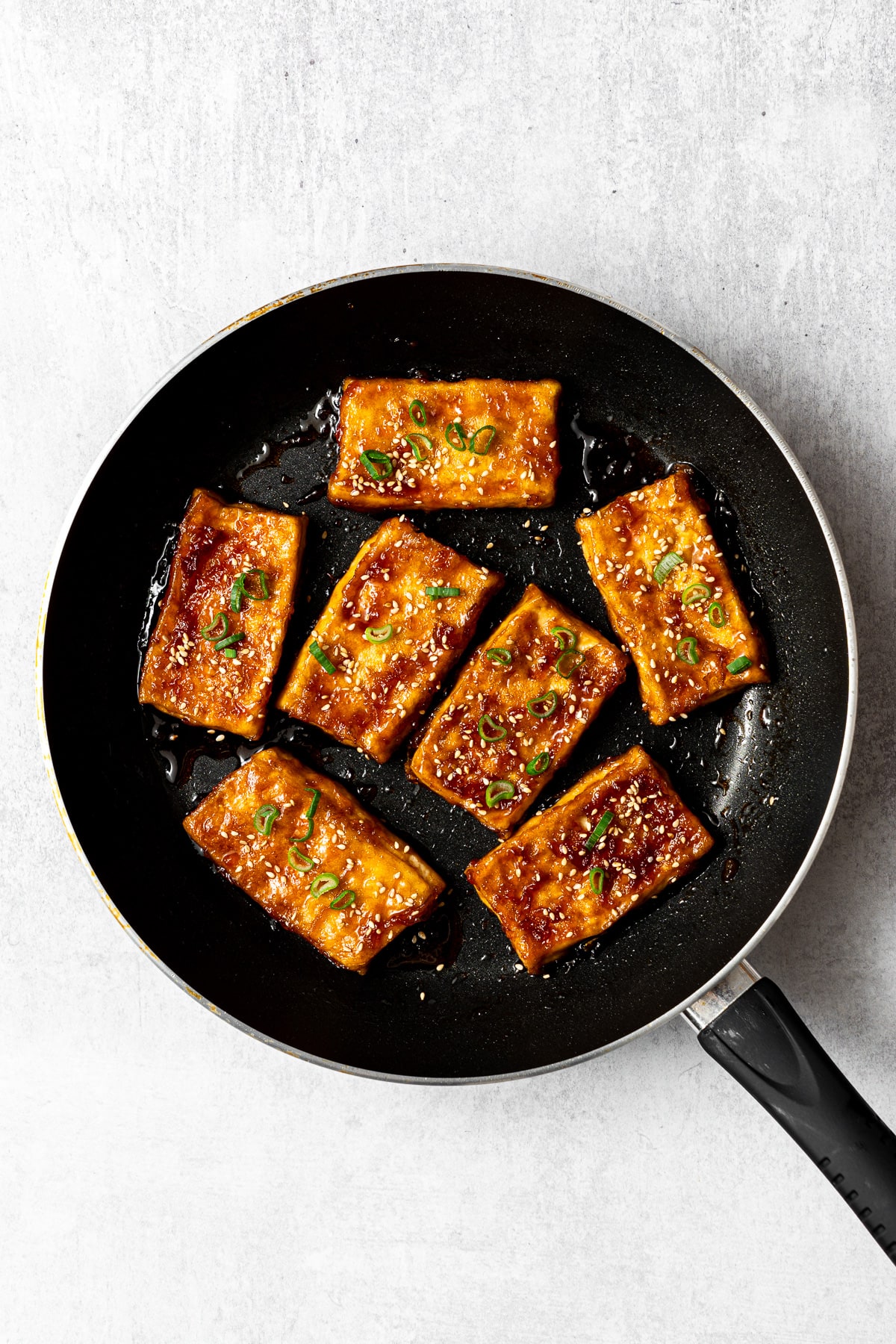 teriyaki tofu garnished with sesame seeds and green onion slices in a pan