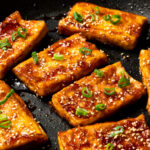 teriyaki tofu garnished with sesame seeds and green onion slices in a pan