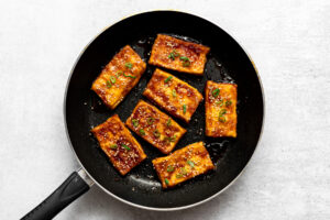 teriyaki tofu garnished with sesame seeds and green onion slices in a pan