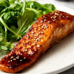 air fryer honey garlic salmon garnished with sesame seeds and a side salad on a plate
