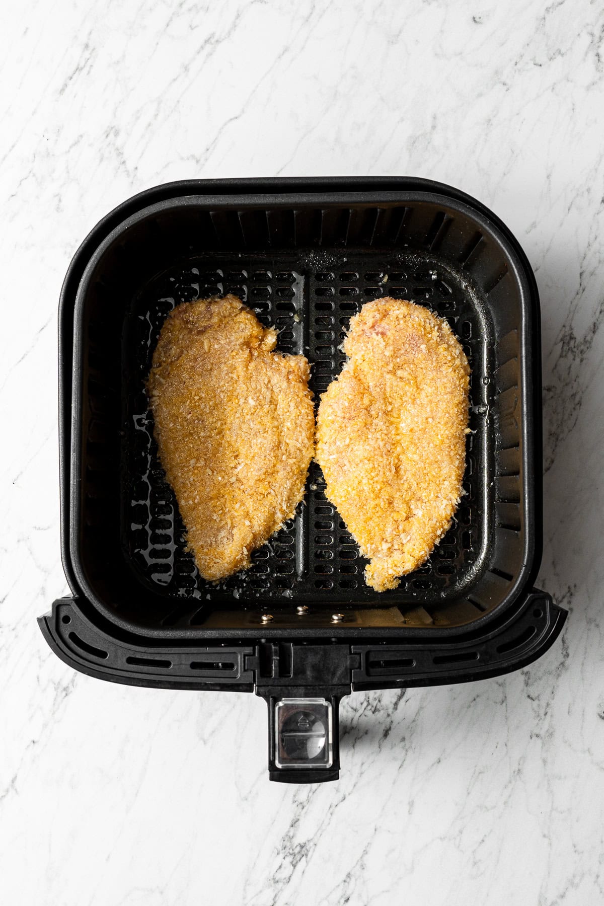 two air fryer parmesan crusted chicken cutlets in an air fryer basket before air frying