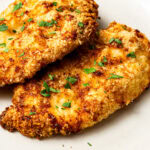 two air fryer parmesan crusted chicken cutlets on a plate garnished with chopped parsley