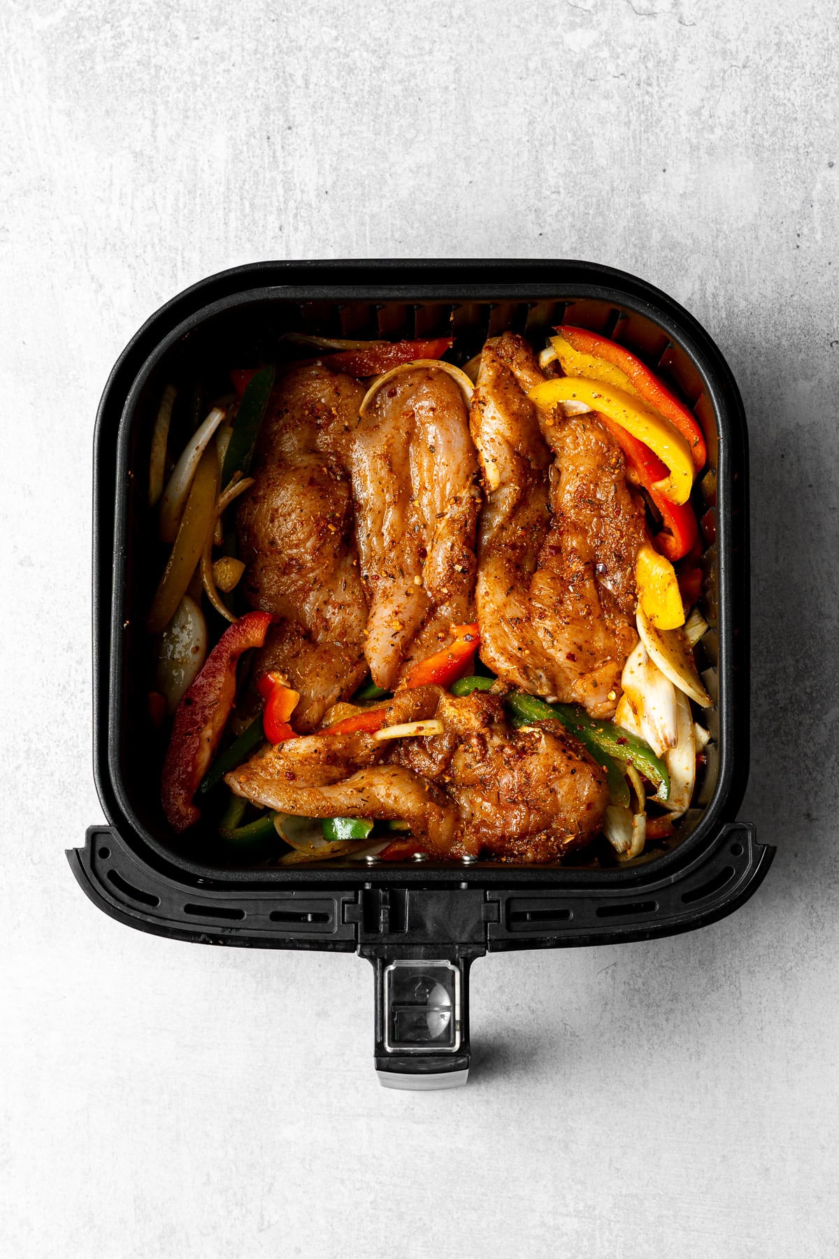 all the ingredients for chicken fajitas in an air fryer basket before cooking