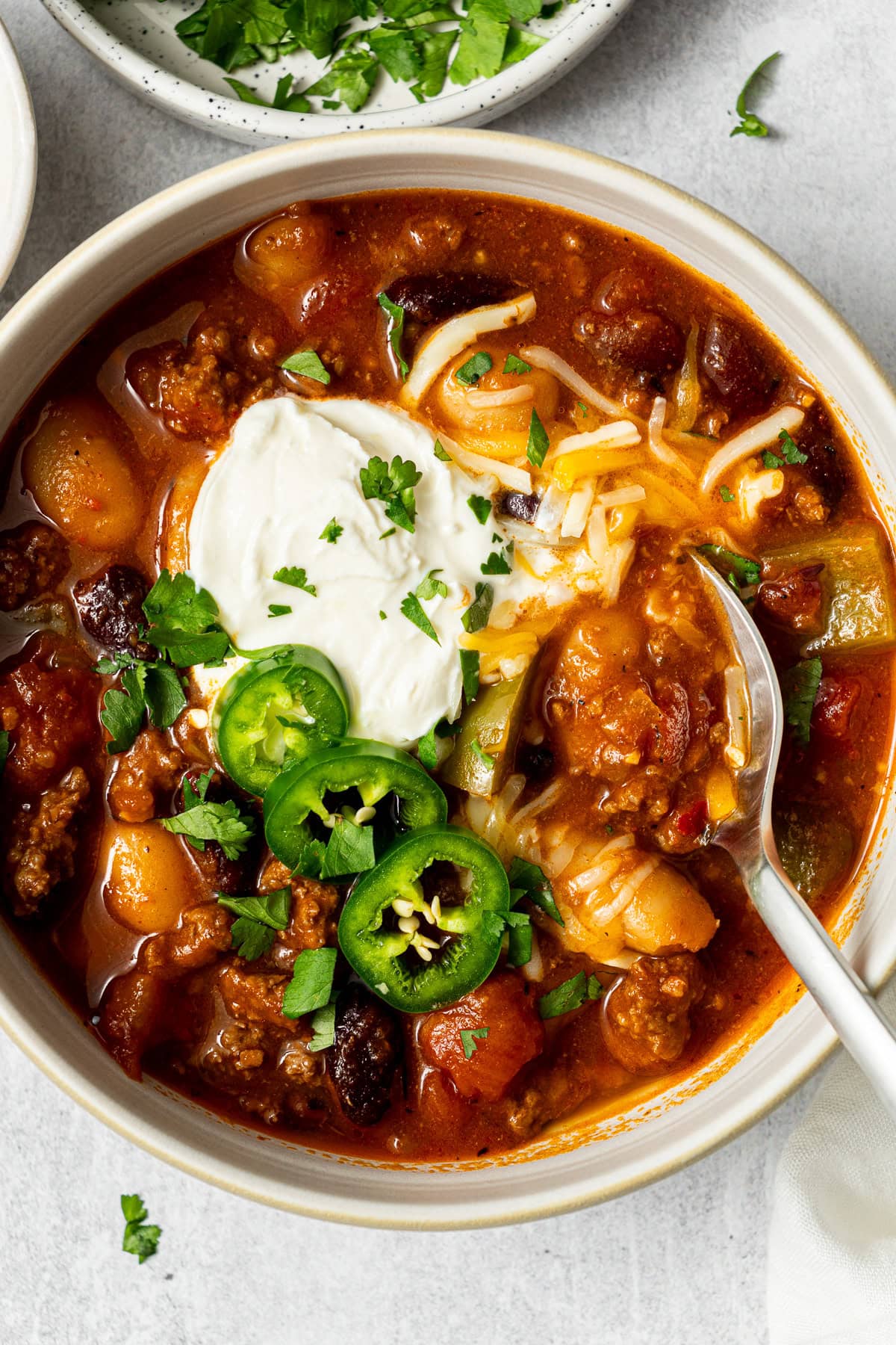 beef pumpkin chili garnished with sour cream, jalapeño slices, shredded cheese, and chopped cilantro in a bowl with a spoon