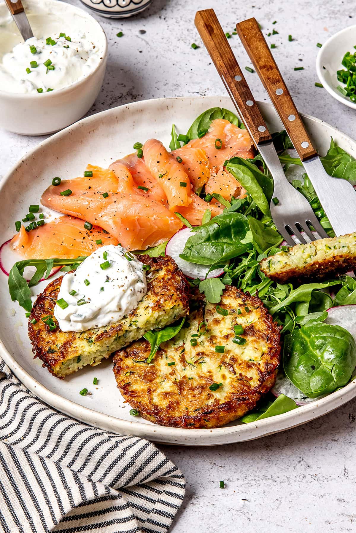 A plate with a smoked salmon, greens and zucchini potato fritters