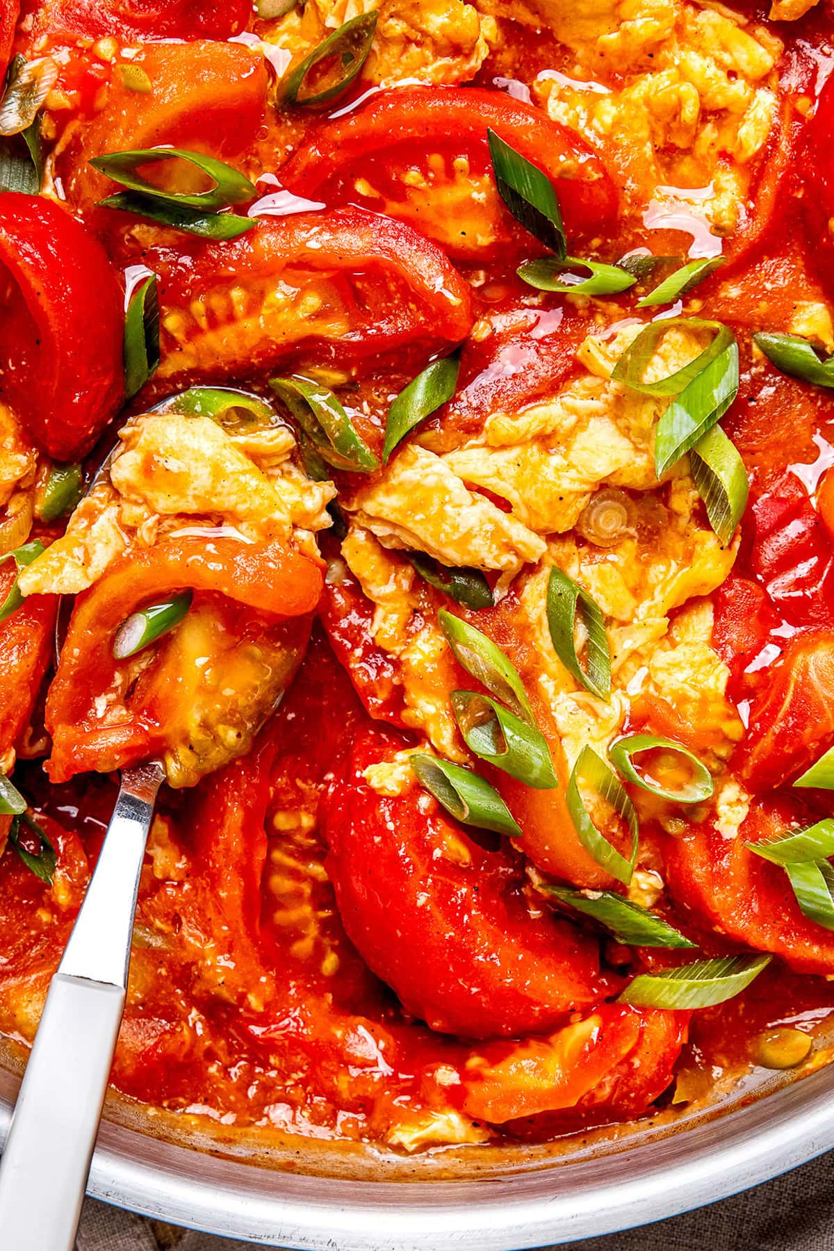 Chinese stir fried tomatoes and eggs in a pan garnished with green onions
