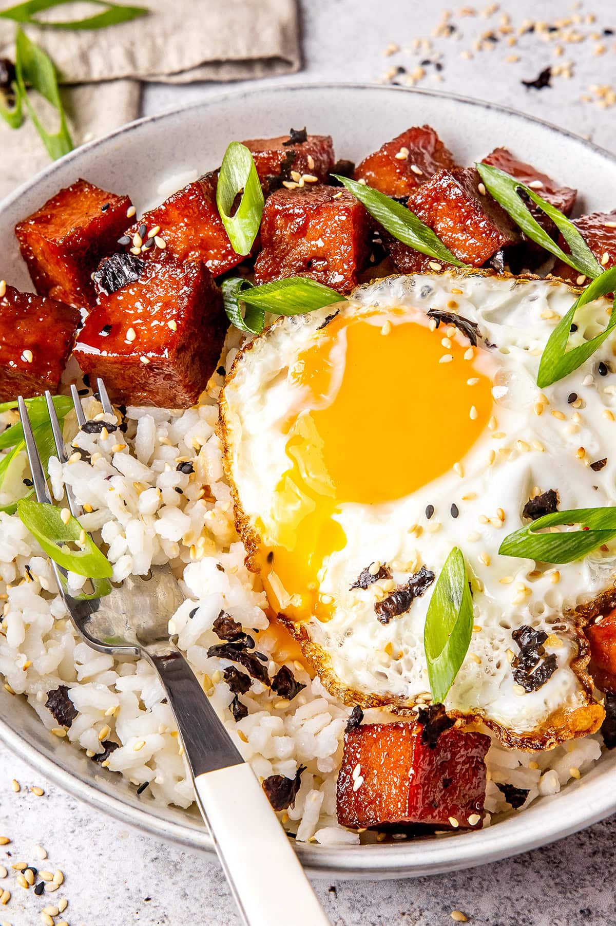 spam and a fried egg served over rice in a bowl garnished with furikake and green onion