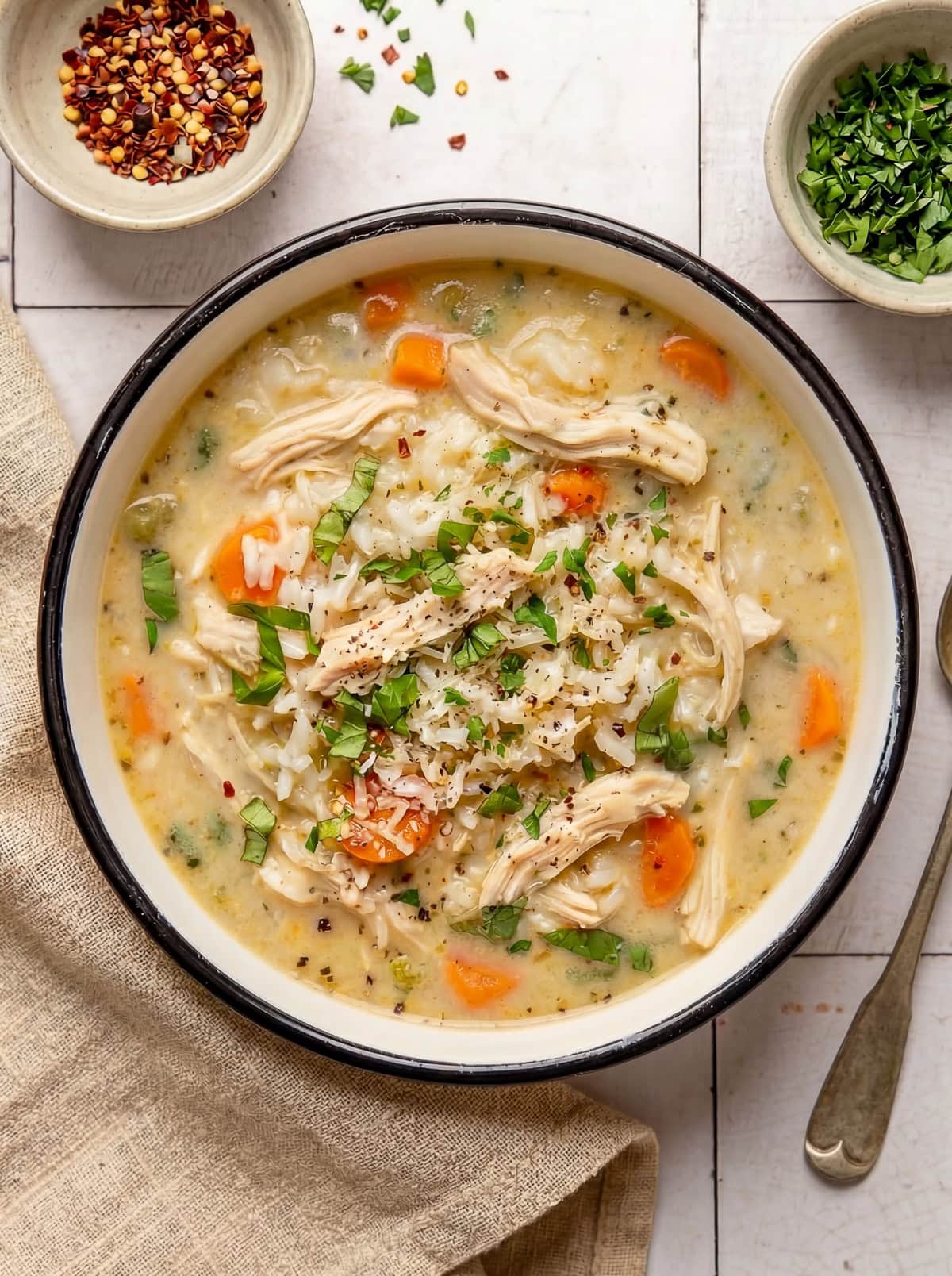 chicken and rice soup in a bowl garnished with chopped parsley and red pepper flakes