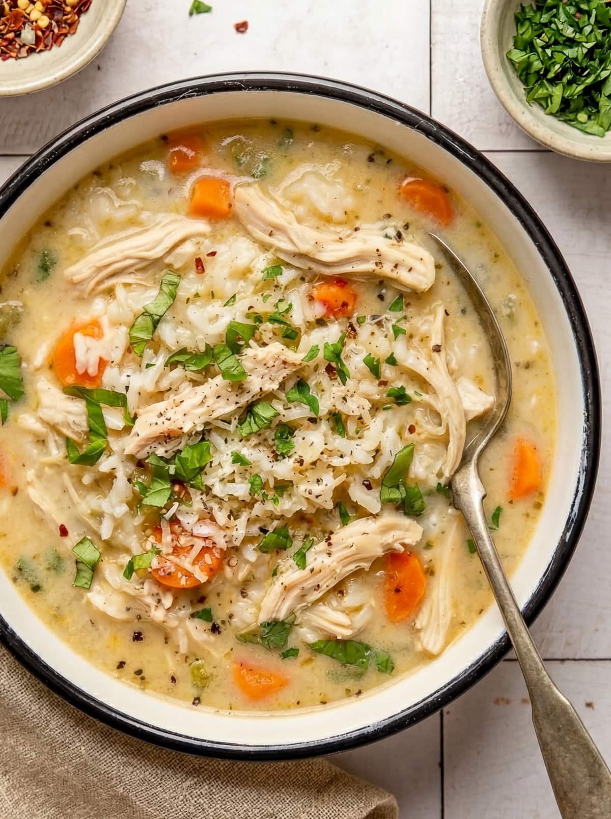 chicken and rice soup in a bowl garnished with chopped parsley and red pepper flakes