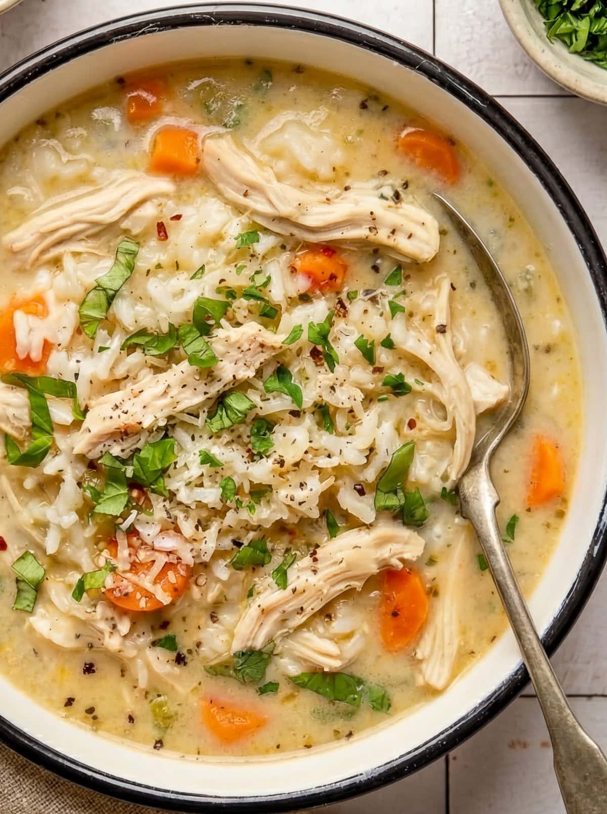 chicken and rice soup in a bowl garnished with chopped parsley and red pepper flakes with a spoon