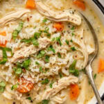 chicken and rice soup in a bowl garnished with chopped parsley and red pepper flakes with a spoon