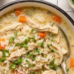chicken and rice soup in a bowl garnished with chopped parsley and red pepper flakes with a spoon