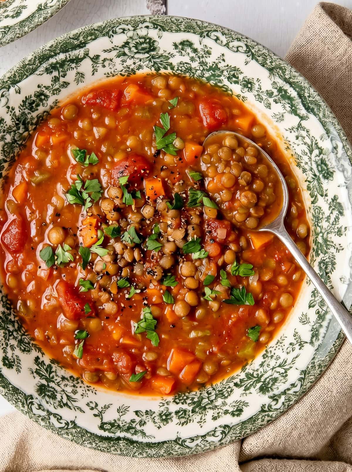 tomato lentil soup in a bowl garnished with chopped parsley and a spoon