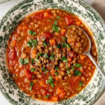 tomato lentil soup in a bowl garnished with chopped parsley and a spoon