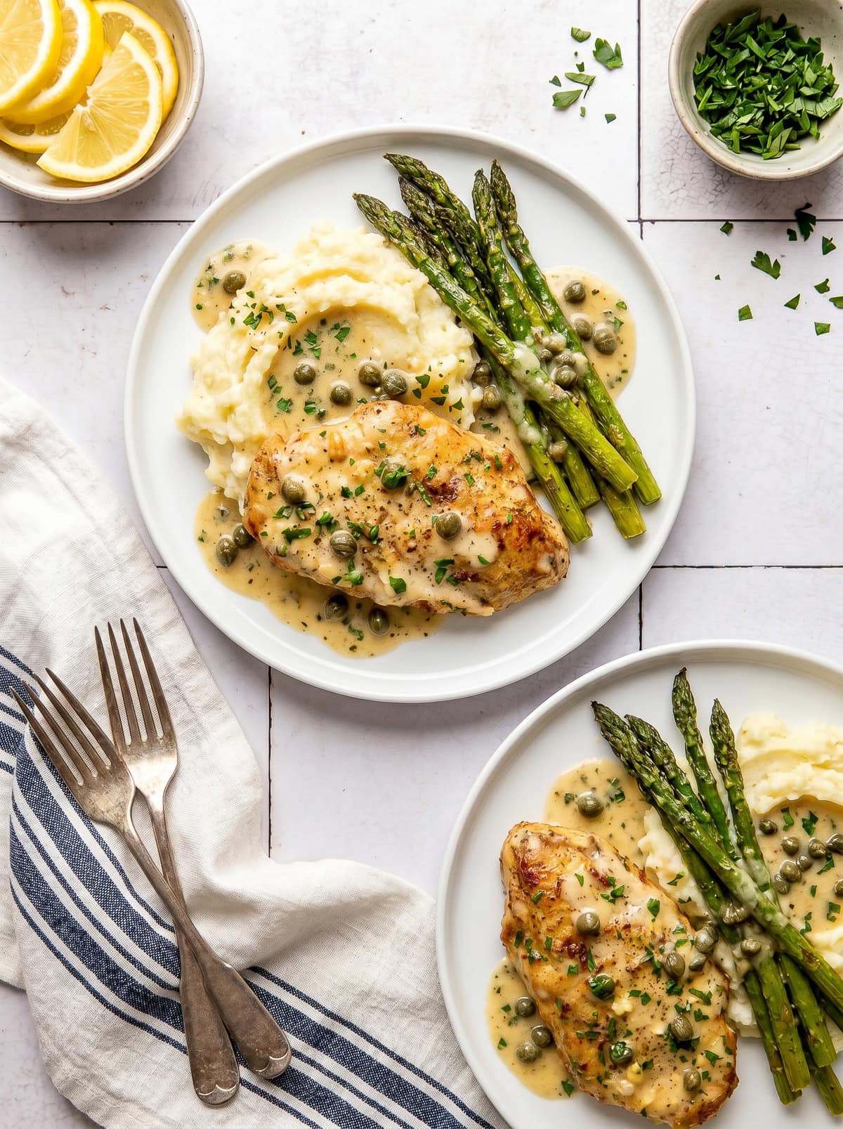 chicken piccata served with mashed potatoes and roasted asparagus on a white plate
