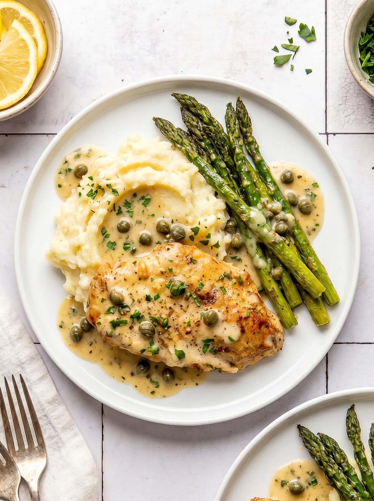 chicken piccata served with mashed potatoes and roasted asparagus on a white plate