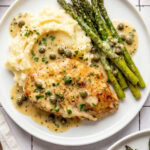 chicken piccata served with mashed potatoes and roasted asparagus on a white plate