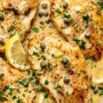 chicken piccata in a pan garnished with chopped parsley