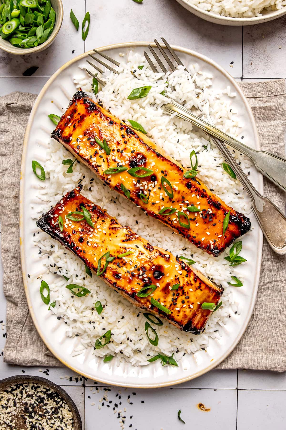 miso glazed salmon served on a long plate with white rice and with two forks