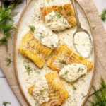 pan seared cod fillets with lemon dill cream sauce on an oval shaped plate with a spoon