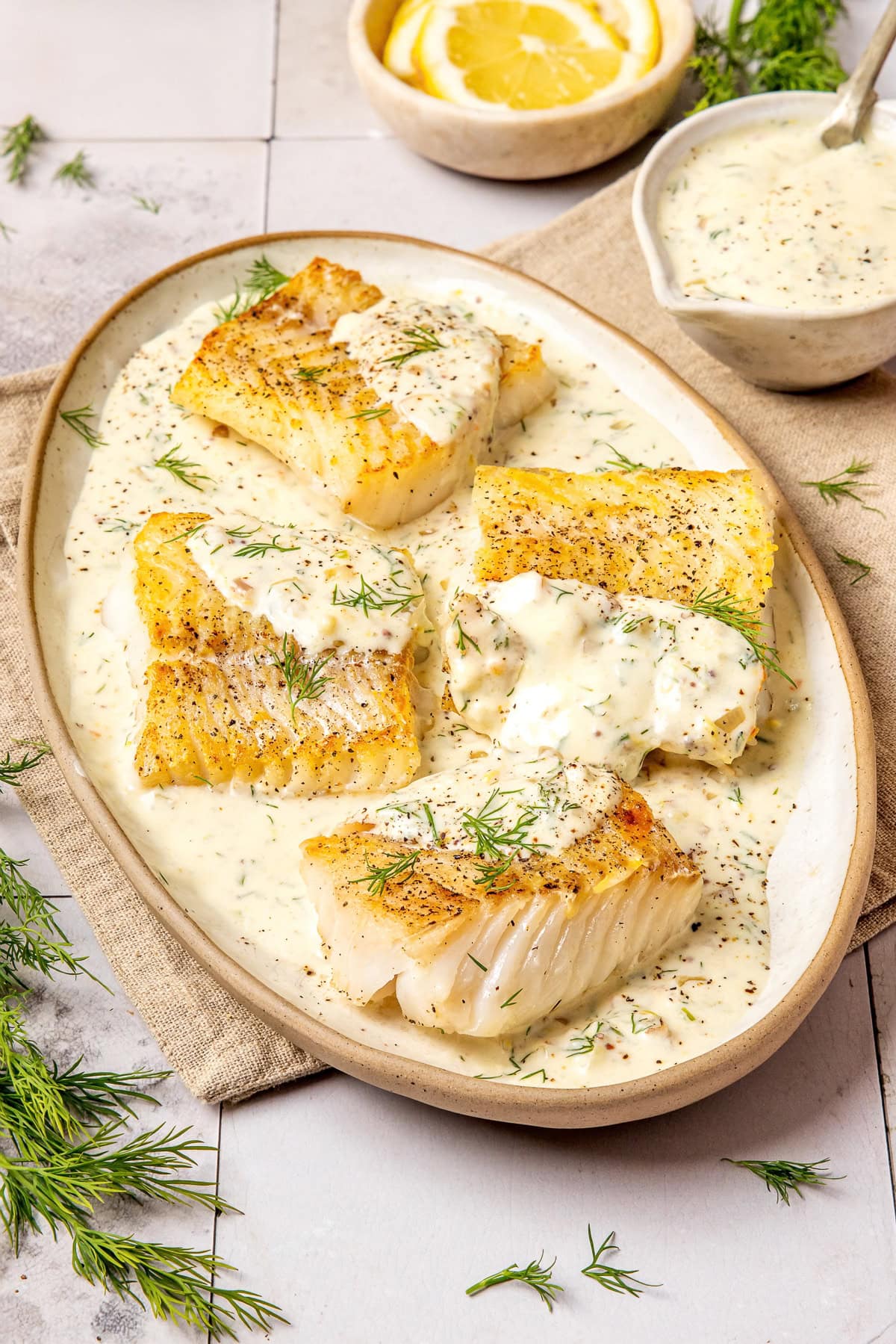 pan seared cod fillets with lemon dill cream sauce on an oval shaped plate