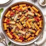 pasta alla norma in a pan garnished with grated parmesan cheese and chopped fresh basil