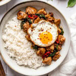 Thai basil chicken served in a bowl with white rice and a fried egg on top