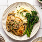 chicken marsala served with mashed potatoes and roasted broccolini on a plate garnished with chopped parsley