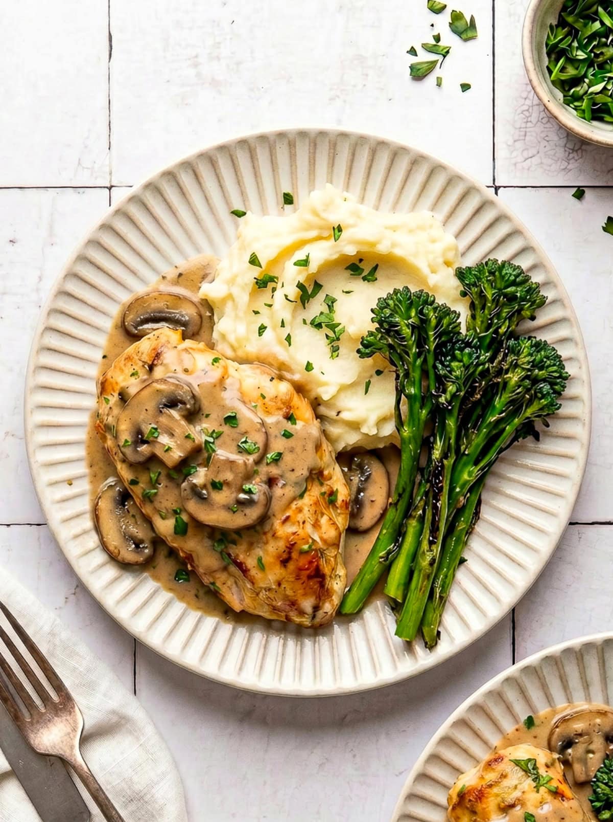 chicken marsala served with mashed potatoes and roasted broccolini on a plate garnished with chopped parsley