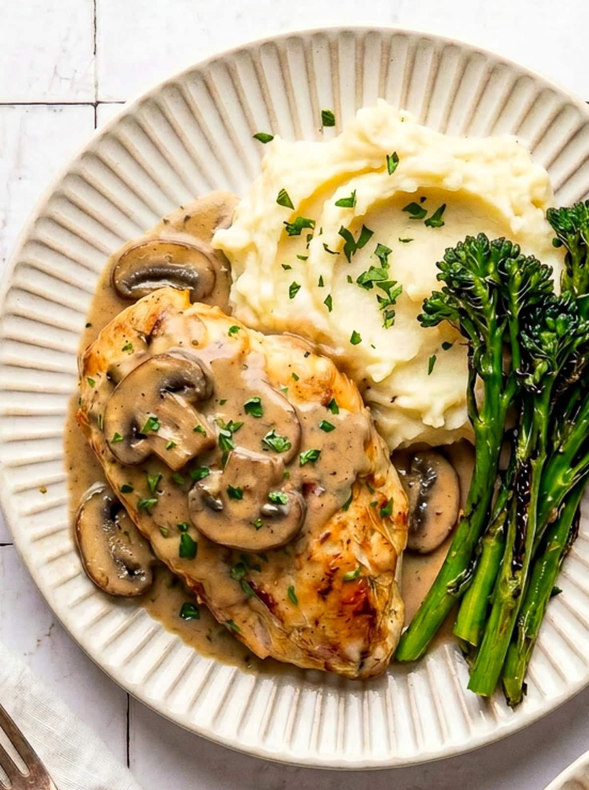 chicken marsala served with mashed potatoes and roasted broccolini on a plate garnished with chopped parsley