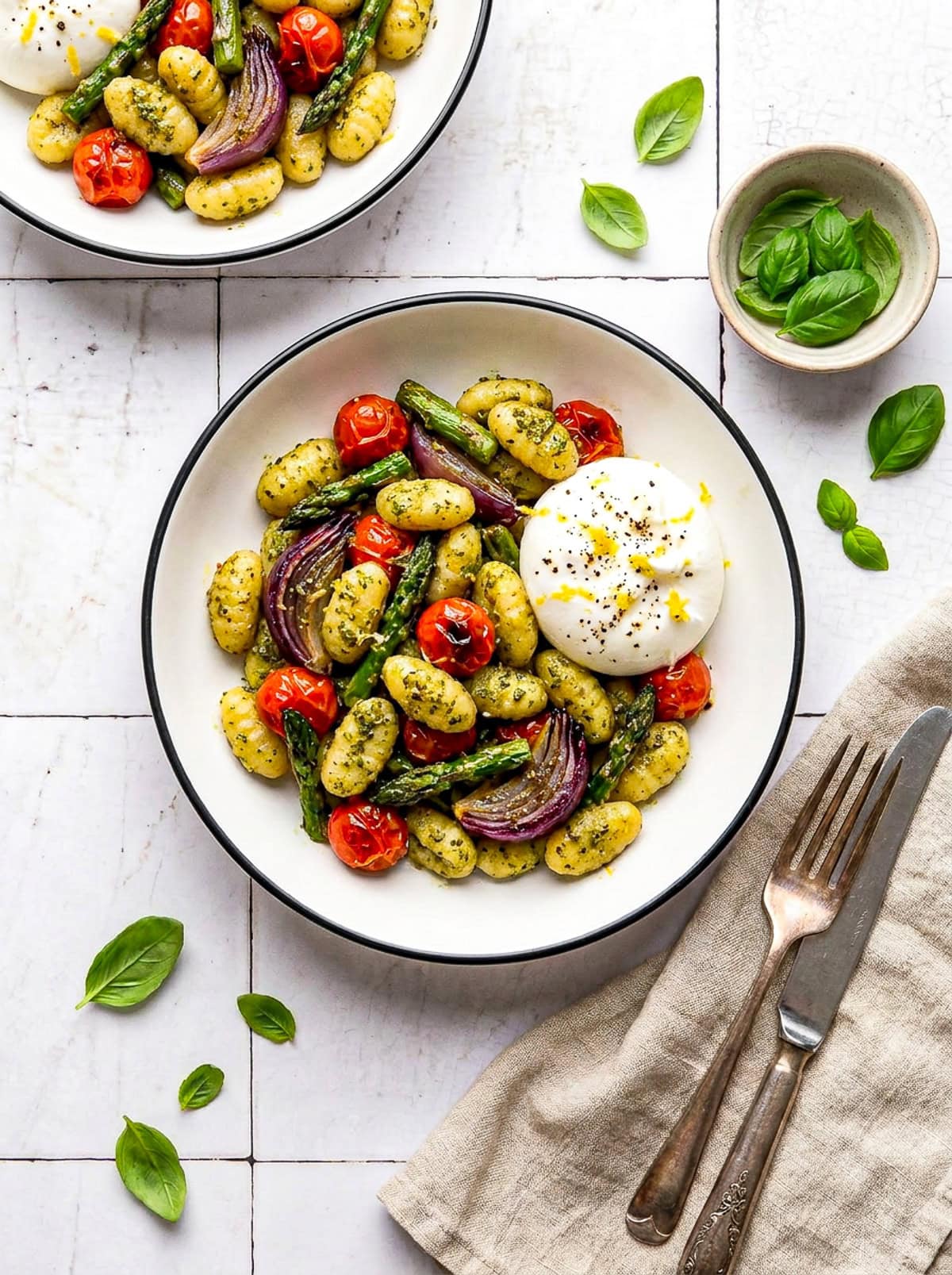 pesto sheet pan gnocchi in a bowl with burrata and garnished with lemon zest and black pepper