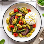 pesto sheet pan gnocchi in a bowl with burrata and garnished with lemon zest and black pepper