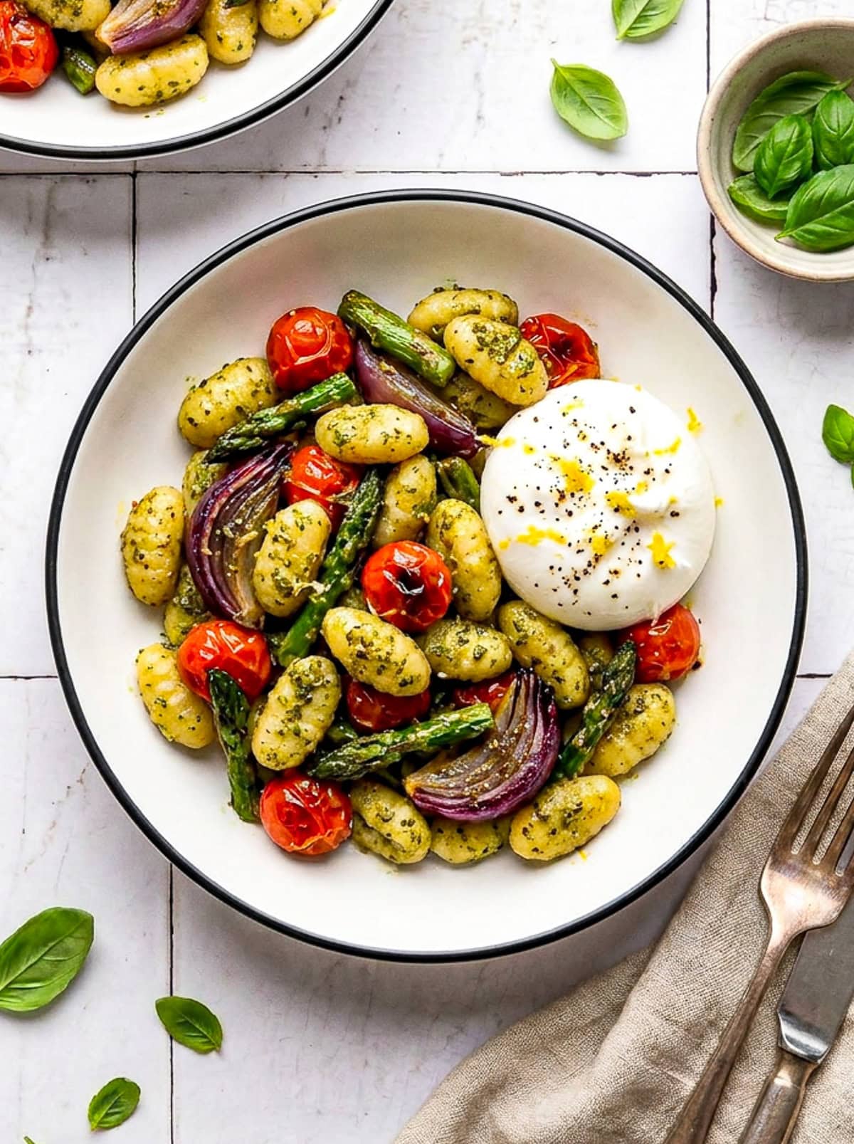 pesto sheet pan gnocchi in a bowl with burrata and garnished with lemon zest and black pepper