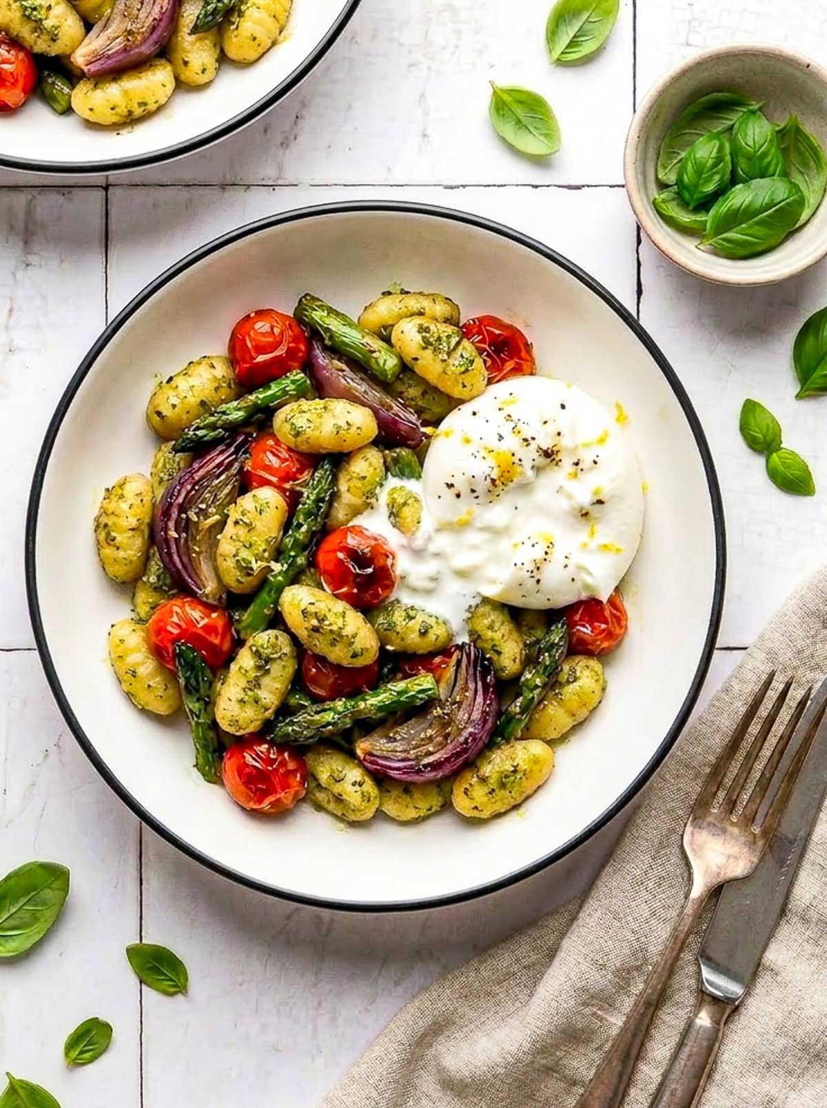 pesto sheet pan gnocchi in a bowl with burrata and garnished with lemon zest and black pepper