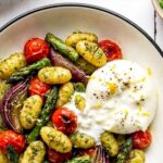 pesto sheet pan gnocchi in a bowl with burrata and garnished with lemon zest and black pepper