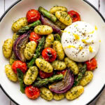 pesto sheet pan gnocchi in a bowl with burrata and garnished with lemon zest and black pepper