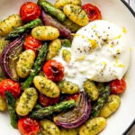 pesto sheet pan gnocchi in a bowl with burrata and garnished with lemon zest and black pepper