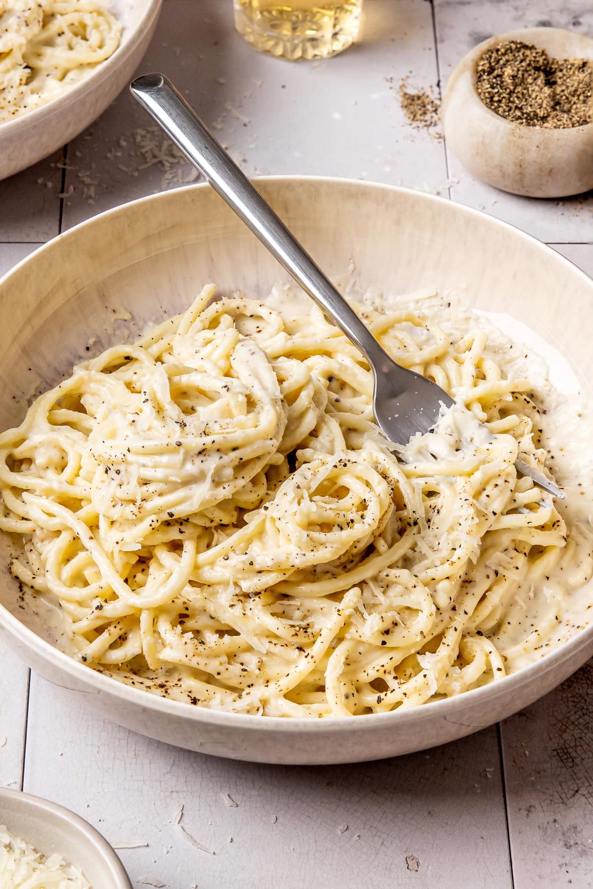 cacio e pepe garnished with black pepper and grated pecorino in a bowl with a fork