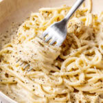 cacio e pepe garnished with black pepper and grated pecorino in a bowl with a fork